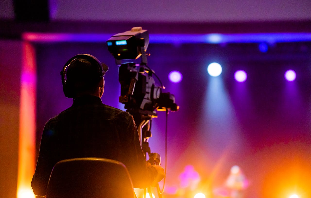 about-img A videographer recording a live concert with vibrant spotlights, using professional equipment.